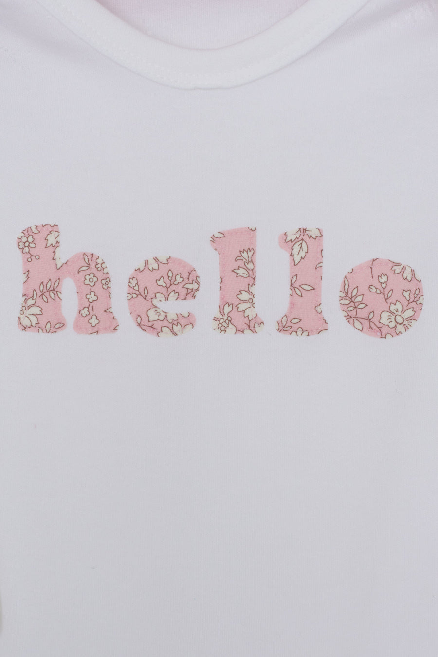 Close up of a white cotton romper with the word hello on it. the letters are cut from Capel floral liberty print and appliquéd onto the romper