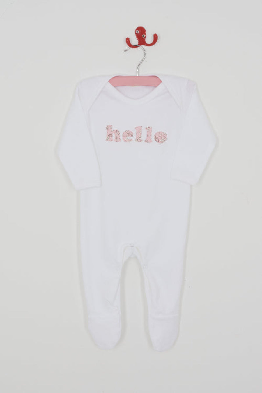Close up of a white cotton romper with the word hello on it. the letters are cut from Capel floral liberty print and appliquéd onto the romper.