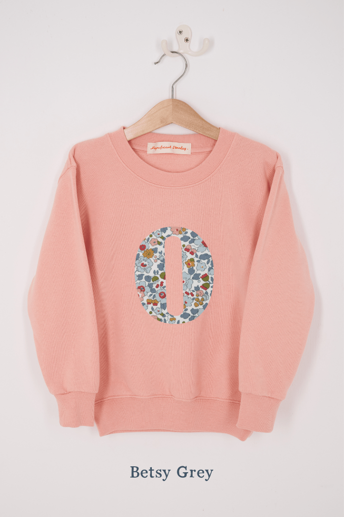 A pink personalised sweatshirt with an initial sewn on to the front. The initial is made from Betsy Grey floral liberty print