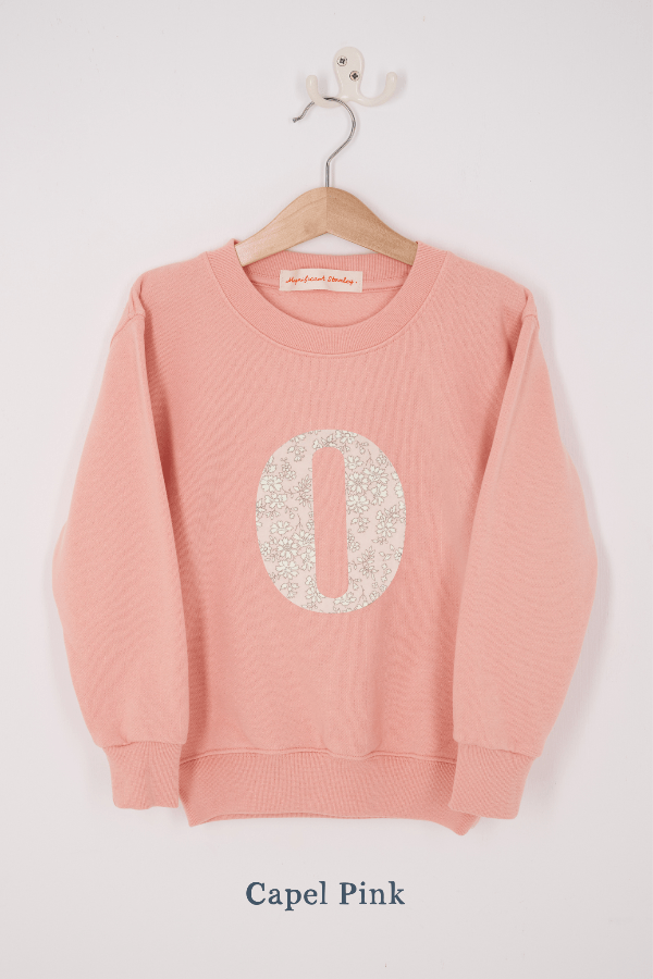 A pink personalised sweatshirt with an initial sewn on to the front. The initial is made from Capel floral liberty print