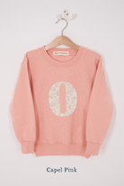 A pink personalised sweatshirt with an initial sewn on to the front. The initial is made from Capel floral liberty print