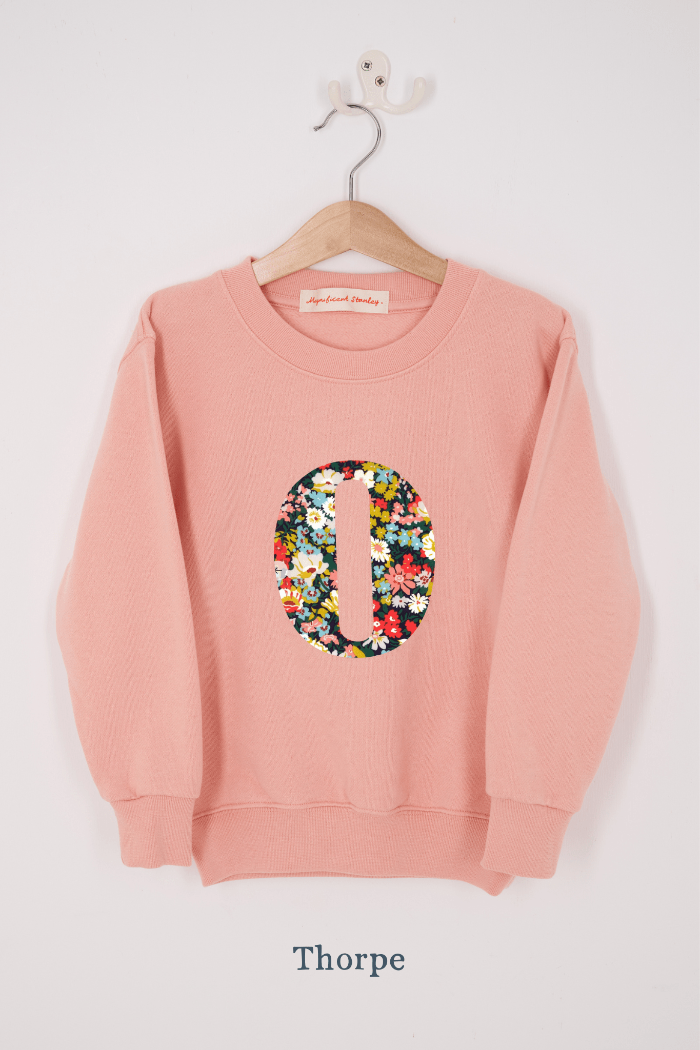 A pink personalised sweatshirt with an initial sewn on to the front. The initial is made from Thorpe floral liberty print.