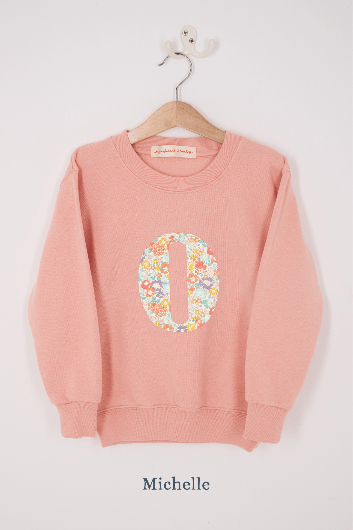 A pink personalised sweatshirt with an initial sewn on to the front. The initial is made from Michelle floral liberty print
