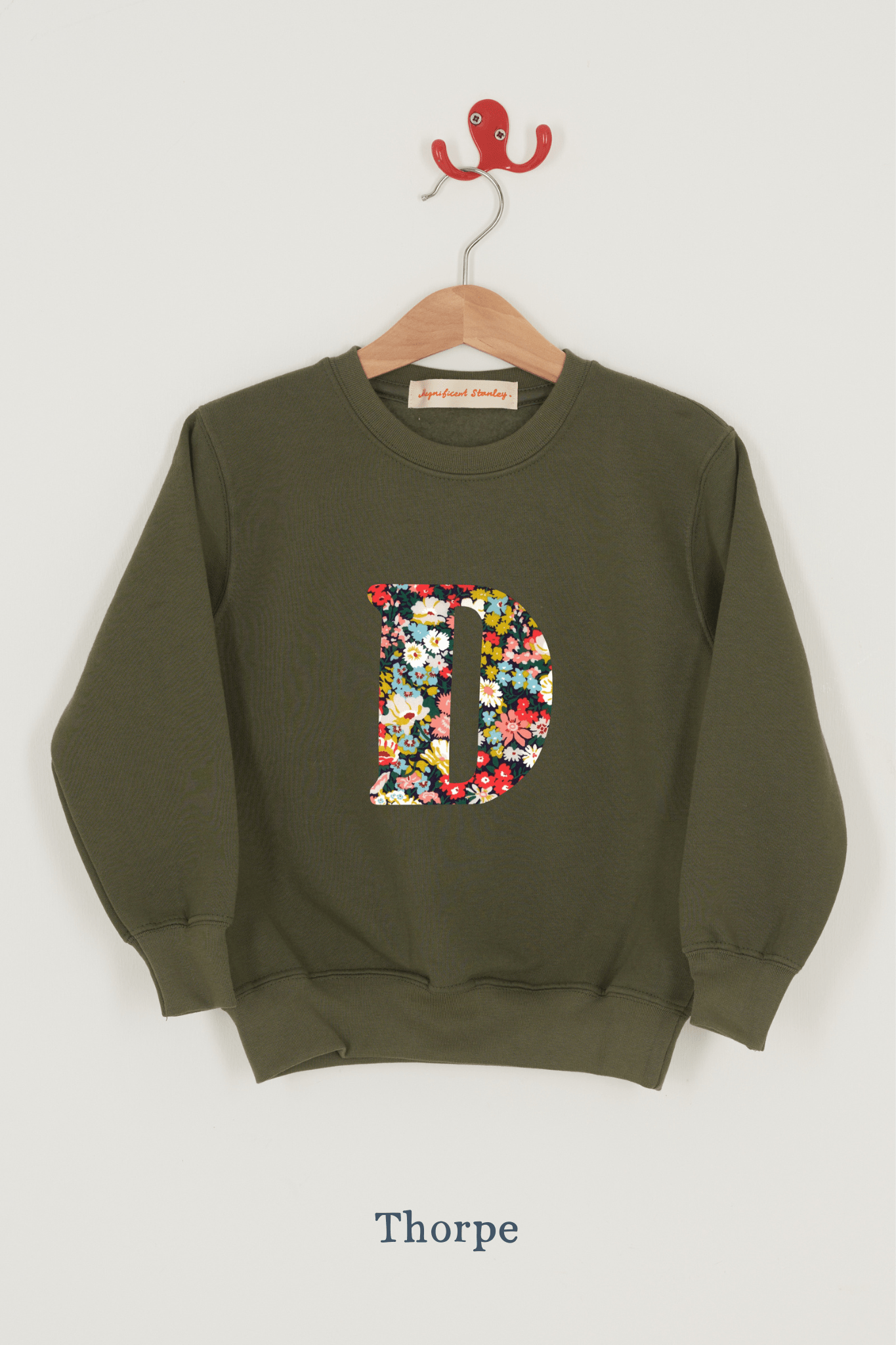 A khaki sweatshirt with an initial on the front. The initial is made from Thorpe floral Liberty print.