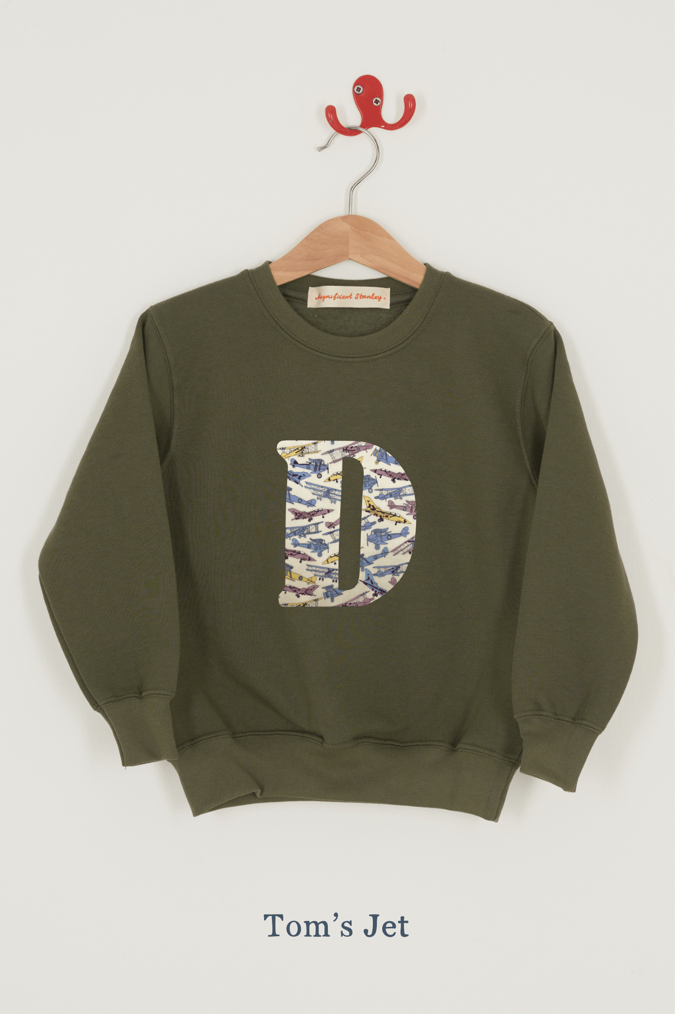 A khaki sweatshirt with an initial on the front. The initial is made from Liberty print featuring vintage jet planes.