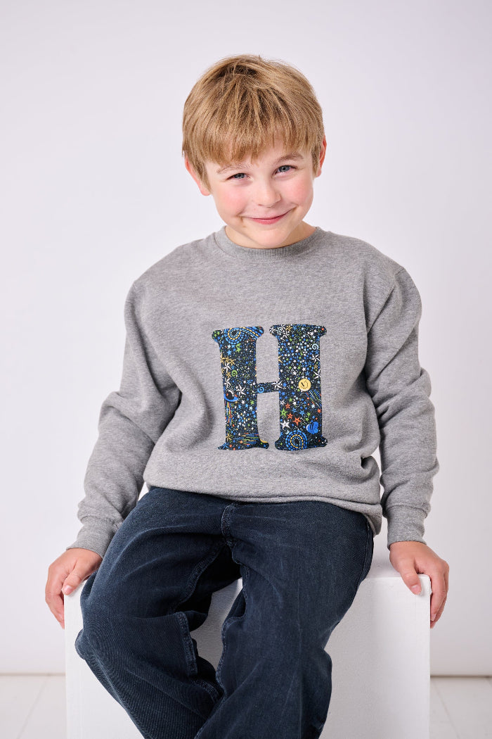 a 7 year old  boy wearing a personalised Magnificent Stanley Grey kids Sweatshirt with his initial on in Adelajda in Space liberty print.