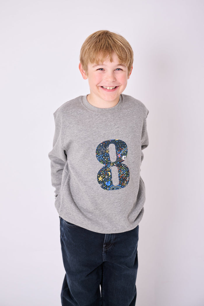 a 7 year old  boy wearing a personalised Magnificent Stanley Grey kids Sweatshirt with his initial on in Adelajda in Space liberty print.