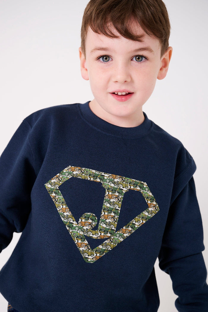 A 5 year old boy in a navy sweatshirt with his initial on the front in a superhero triangle cut from Liberty cars fabric.