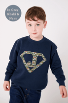 A 5 year old boy in a navy sweatshirt with his initial on the front in a superhero triangle cut from Liberty cars fabric.