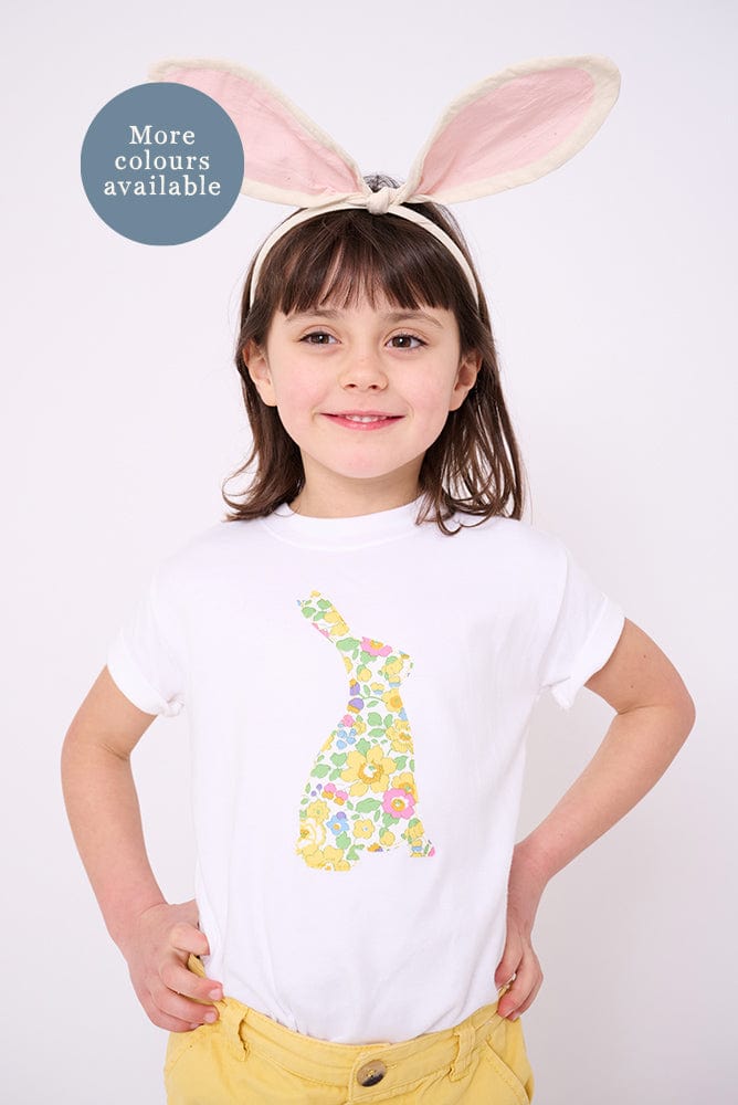 A smiling girl wearing a white cotton t-shirt with a floral liberty print bunny on the front and she has bunny ears on her head.
