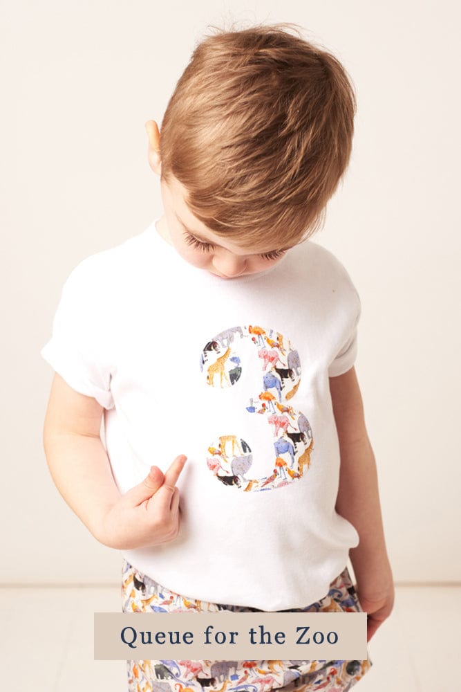 A 3 year old boy wearing a personalised white cotton t-shirt with his initial on in Queue for the Zoo Liberty fabric.