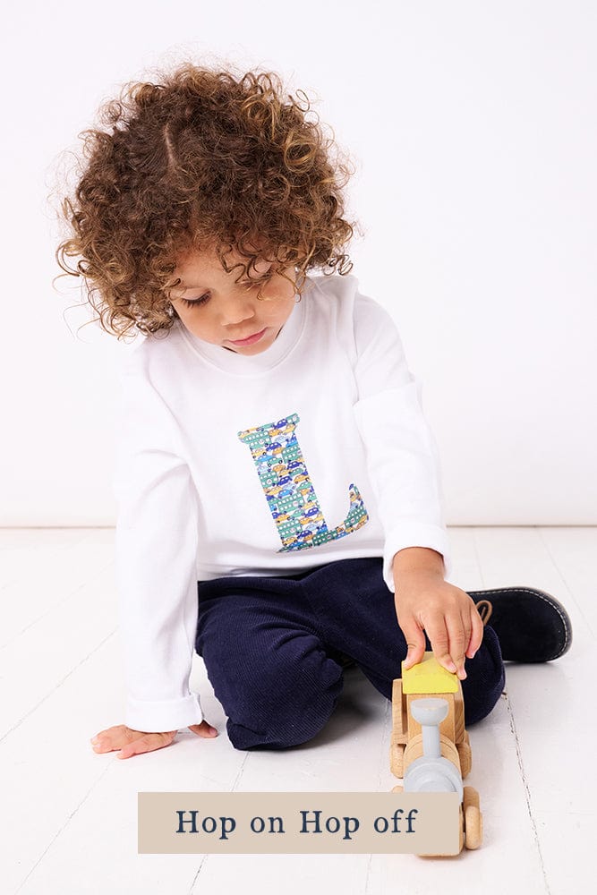 A 2 year old boy wearing a personalised white cotton t-shirt with his initial on in Hop On Hop Off Liberty fabric.
