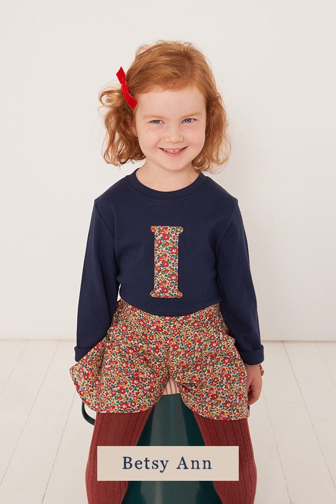 a 4 year old girl wearing a personalised kids navy t-shirt with an initial cut from betsy and liberty print on the front.