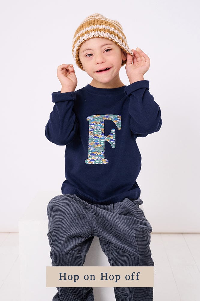 a 4 year old boy wearing a personalised kids navy t-shirt with an initial cut from hop on hop off liberty cars print on the front
