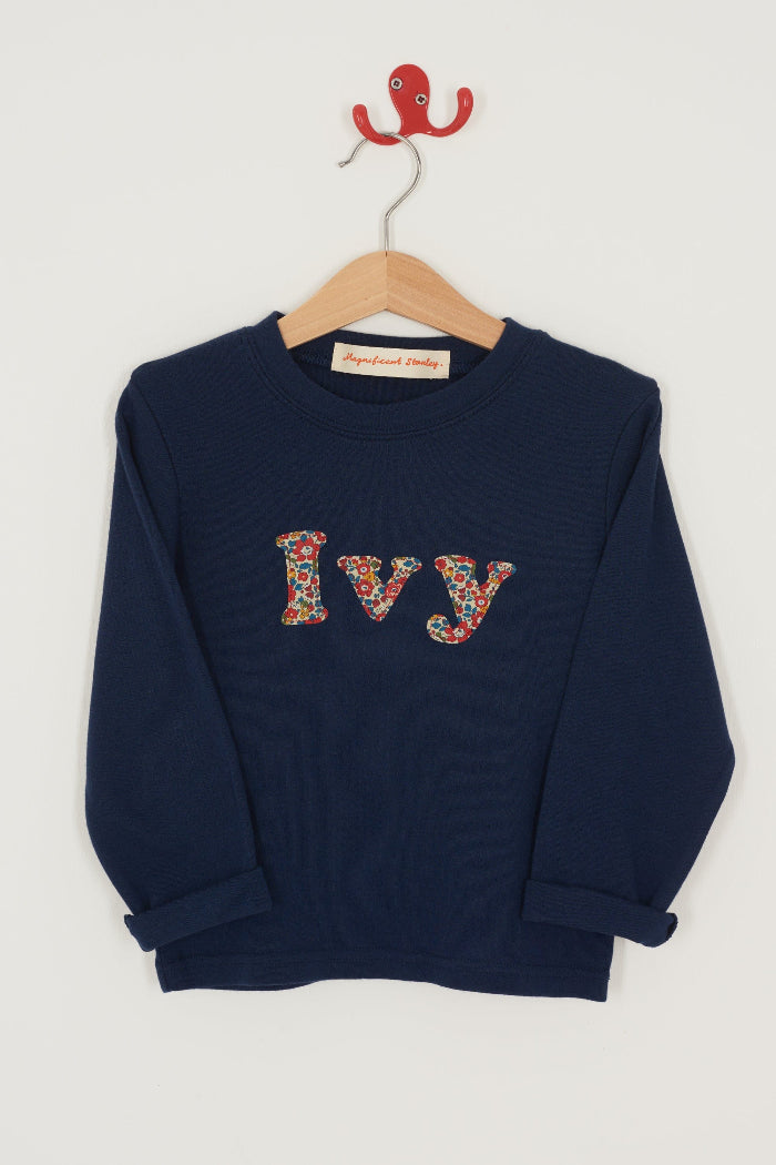 A personalised navy cotton t-shirt with the name Ivy on the front. The name is appliquéd in lowercase letters in Liberty floral fabric.