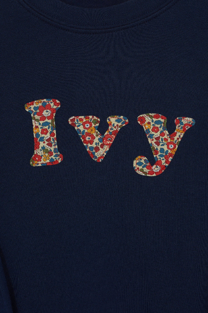 A personalised navy cotton t-shirt with the name Ivy on the front. The name is appliquéd in lowercase letters in Liberty floral fabric.