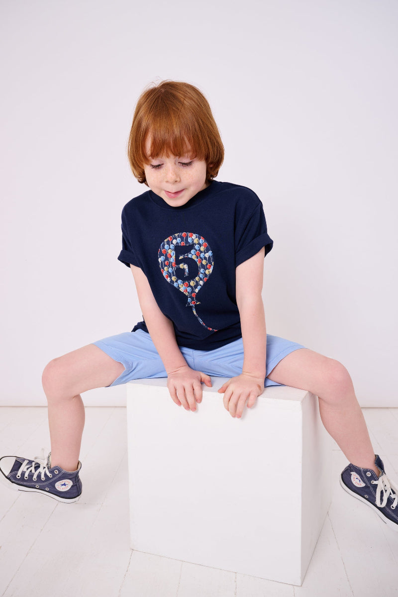 A 5 year old birthday boy wearing a navy t-shirt with a number 5 in a balloon on the front. The balloon is cut from Ethan's Party balloon Liberty print.