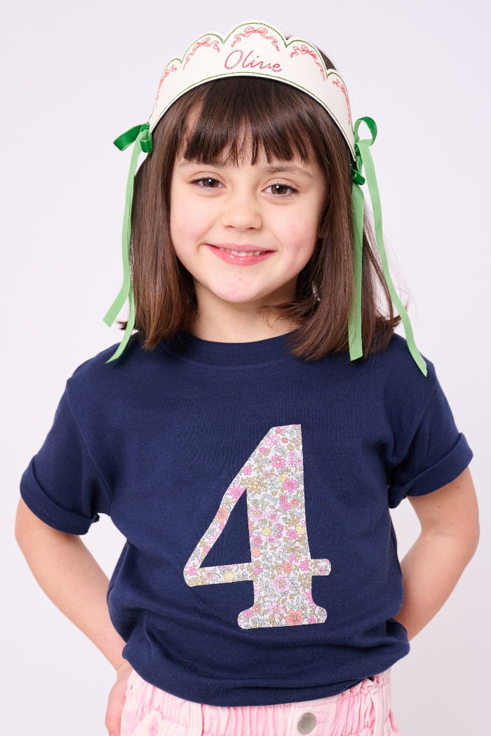 a 4 year old girl wearing a Magnificent Stanley kids Number Navy T-Shirt in Fruit Punch Liberty Print. She also wears an embroidered crown with her name on.