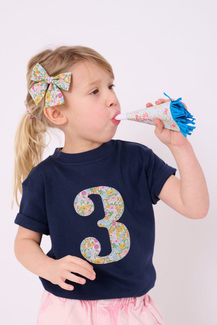 A 3 year old birthday girl wearing a Magnificent Stanley kids Number Navy T-Shirt in Poppy Forest Liberty Print.