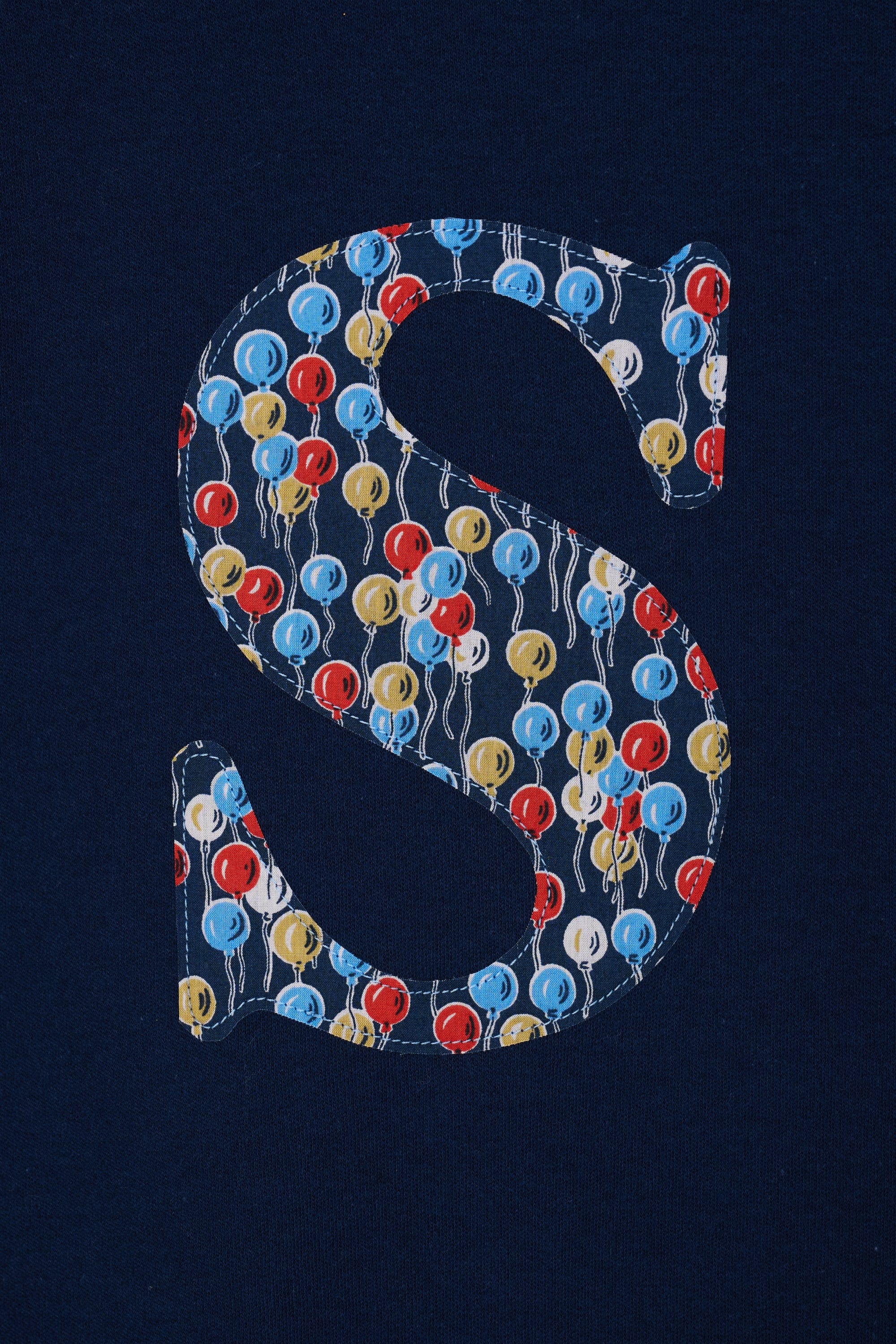 A close up of a navy cotton personalised t-shirt with an initial in Liberty balloon print.