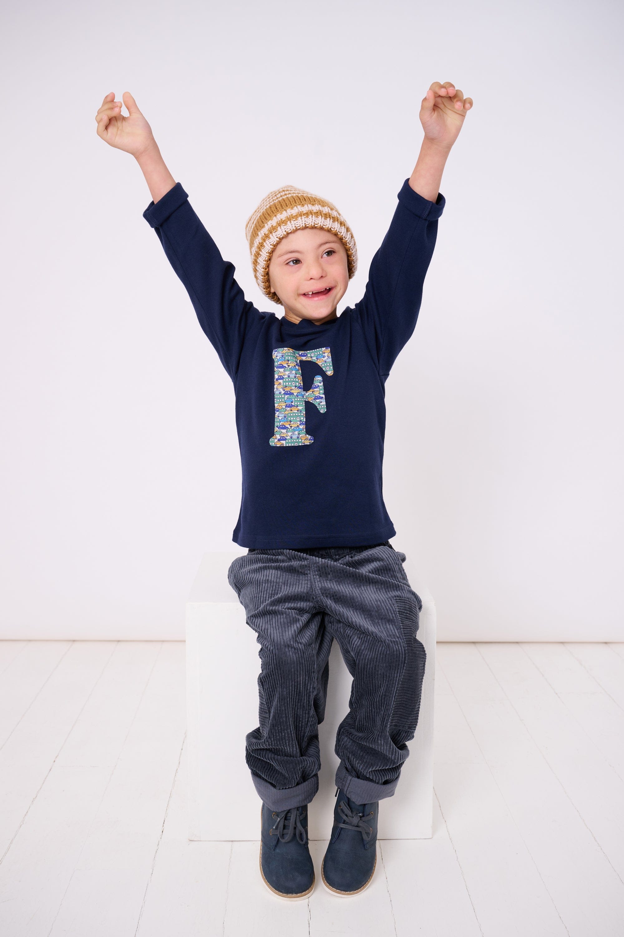 A happy 5 year old child wearing a personalised cotton long sleeve navy t-shirt  with his initial on the front made from Liberty cars print.