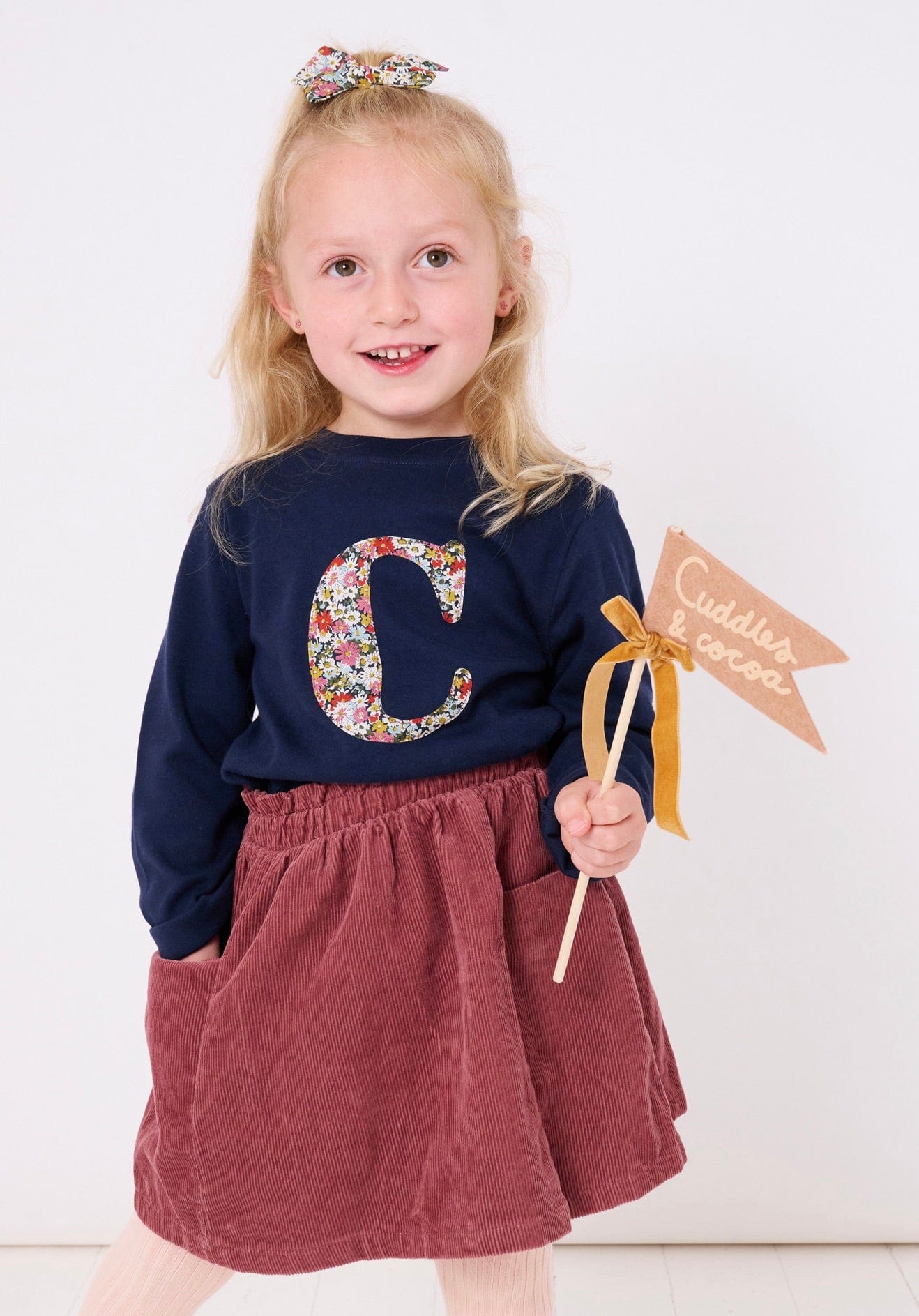 A 3 year old girl wearing a personalised cotton navy long sleeve t-shirt with her initial on the front made from Libby a floral Liberty print.