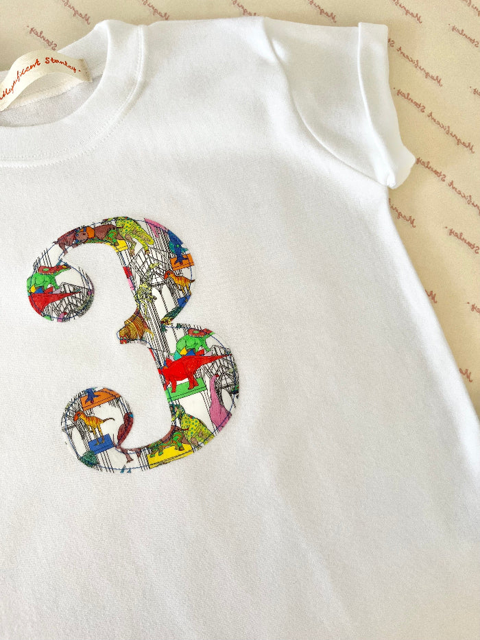 A white kids T-Shirt with a number 3 on the front in Dinosaur Liberty Print