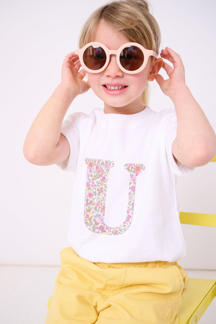 a child wearing a personalised white cotton T-Shirt with her initial letter on the front in Fruit Punch Liberty Print.