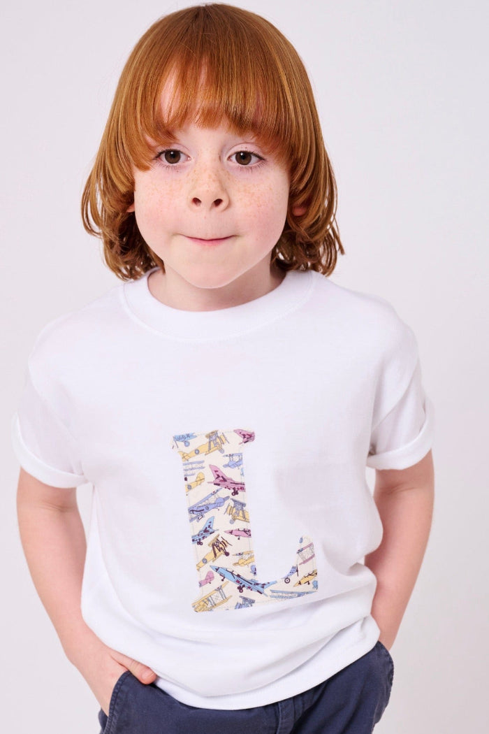 A boy wearing a personalised white cotton T-Shirt with his initial letter on the front in Toms Jet plane Liberty print