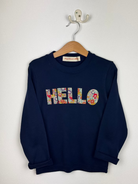 Navy blue sweatshirt with floral 'HELLO' text on a hanger against a white background