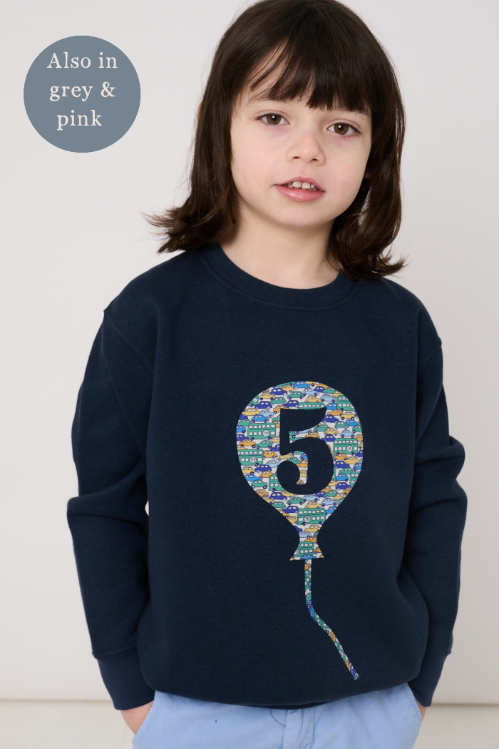 Child wearing a navy blue sweatshirt with a colourful liberty print balloon design featuring the number 5.