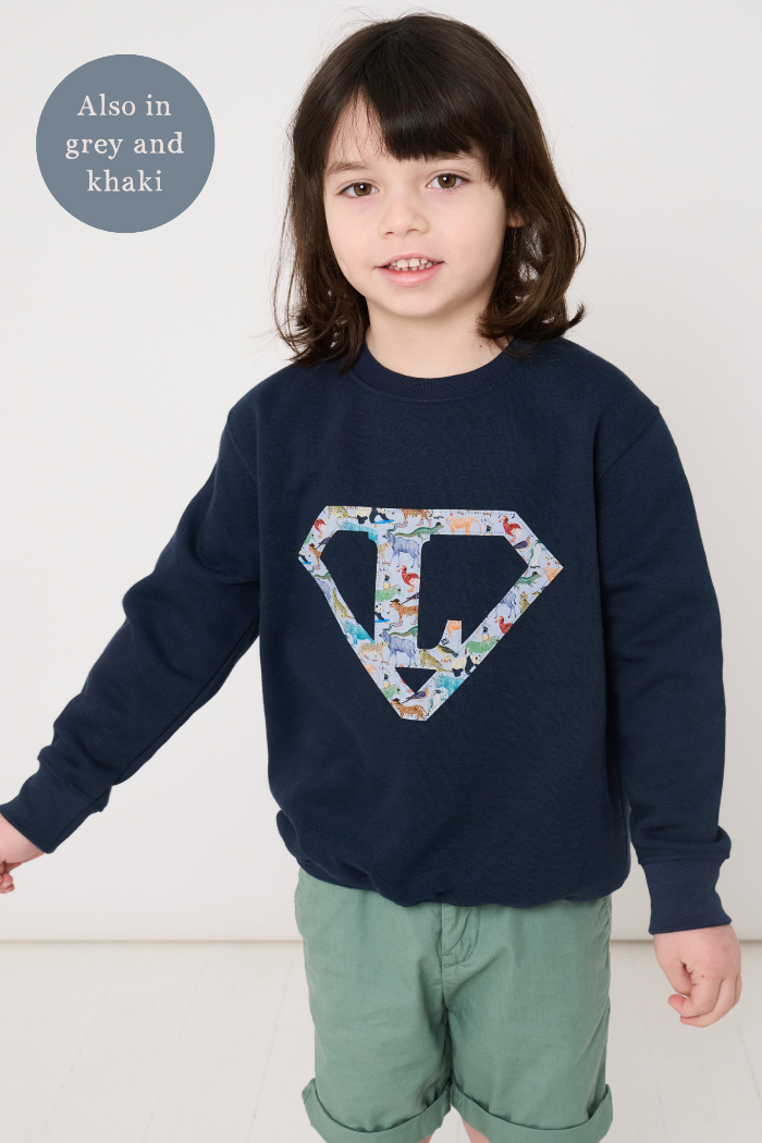 Child wearing a personalised navy blue sweatshirt with an initial superhero logo on the front in Quey 2 animal liberty print