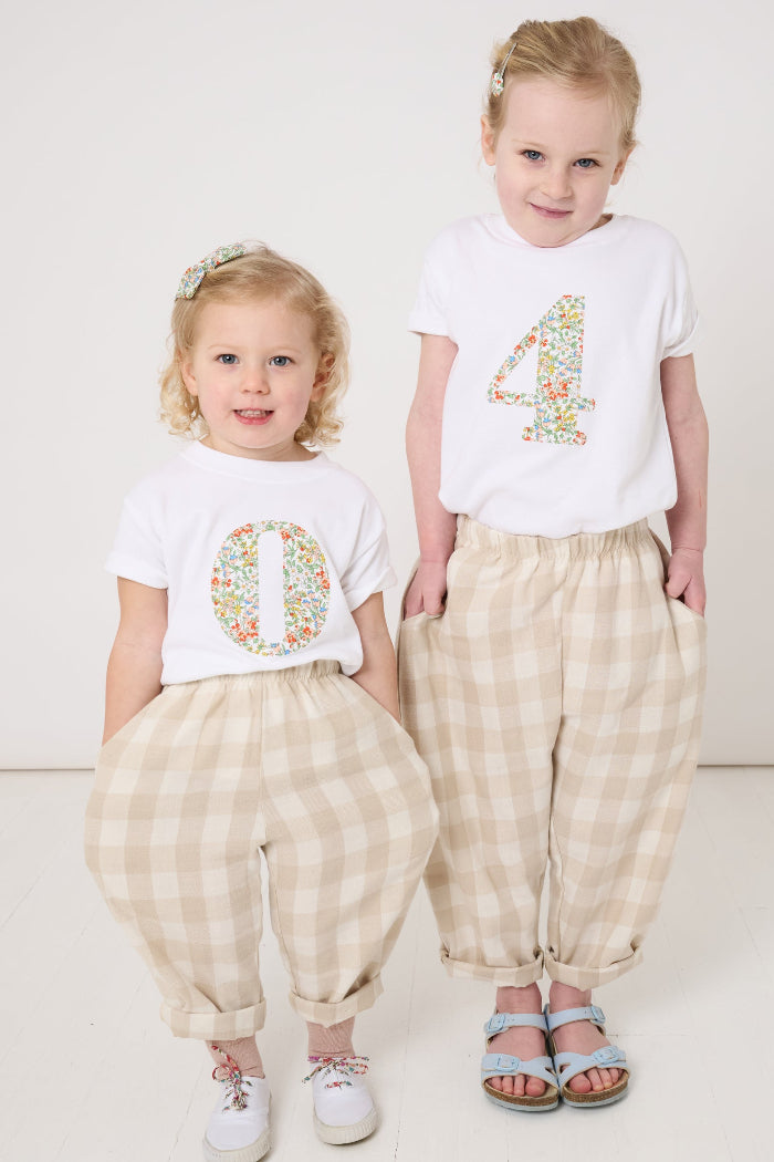 A 2 year old and  a 4 year old wearing matching summery personalised white cotton t-shirts with an initial cut from Nazanin floral liberty fabric.