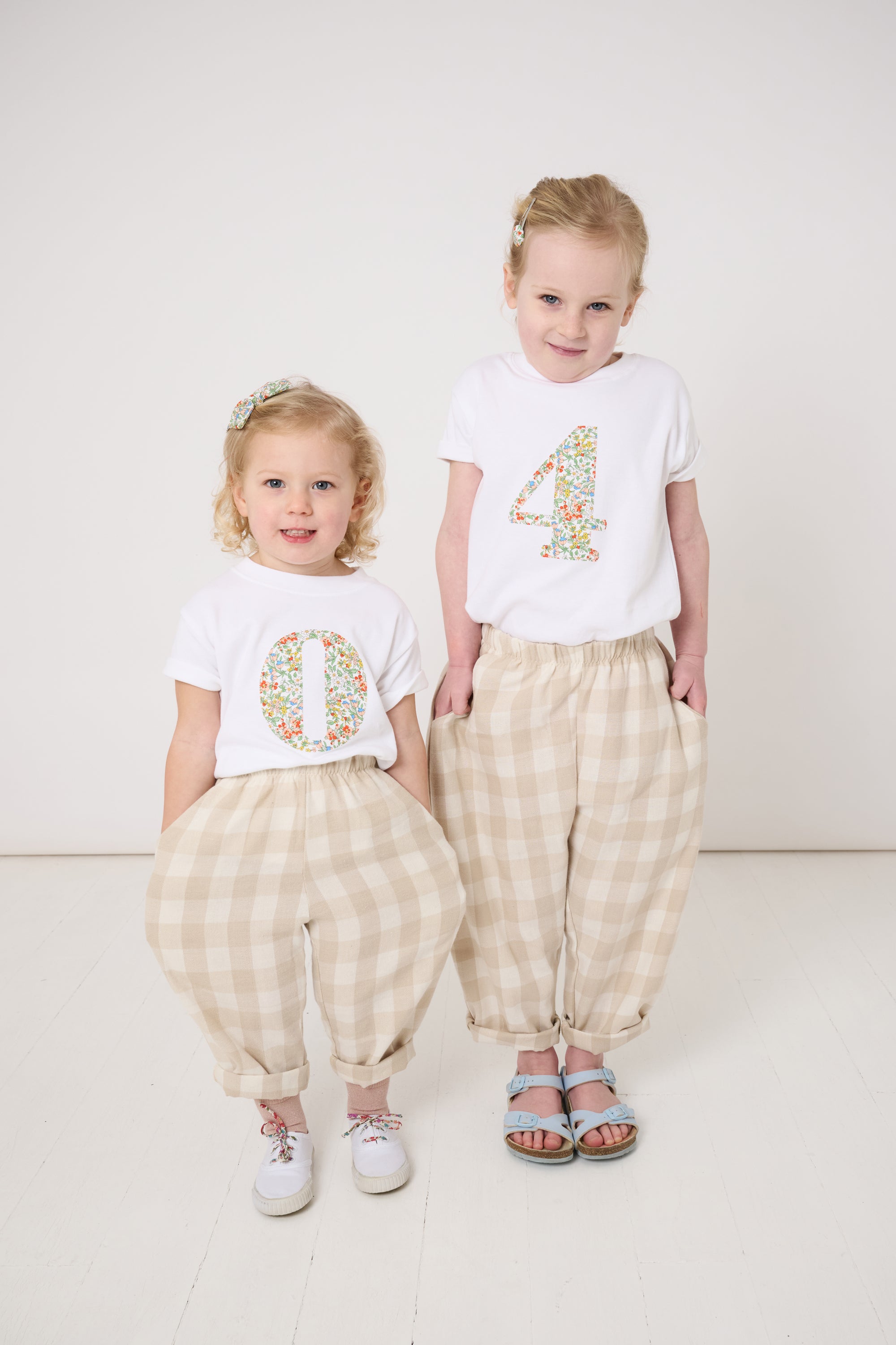 A 4 year old girl wearing a white cotton birthday t-shirt with the number 4 sewn on the front cut from liberty Nazanin fabric. She is in a matching outfit with her little sister.