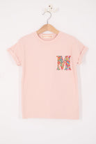 Pink t-shirt with a colorful letter 'M' on a hanger against a white background