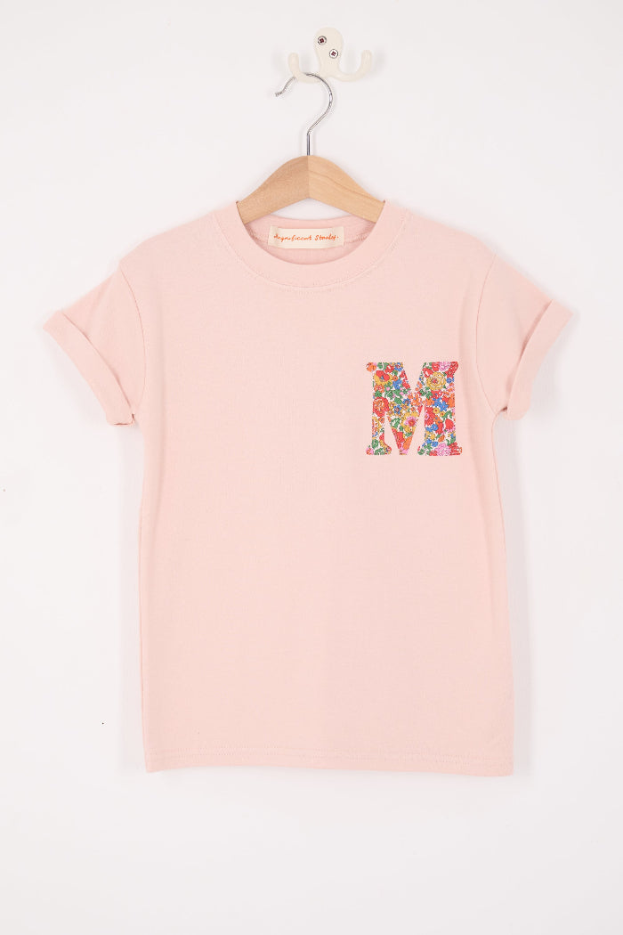Pink t-shirt with a colorful letter 'M' on a hanger against a white background