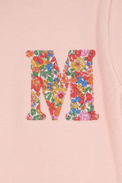 a pale pink t-shirt with a Liberty Nell Annie and May floral small initial on the front, a close up of the stitching