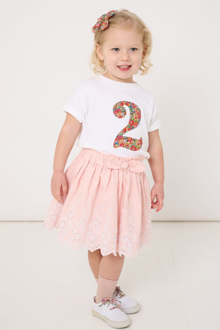 A 2 year old girl wearing a white cotton birthday t-shirt with the number 2 sewn on the front cut from liberty Nell Annie and May fabric.