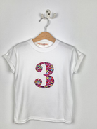 White t-shirt with colorful number '3' design on a hanger against a white background