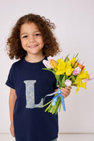 a  3 year old boy wearing a personalised kids navy t-shirt with an initial cut from brave noah dragons print on the front. He is holding a bunch of flowers
