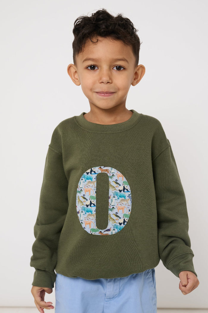 Child wearing a personalised khaki sweater with a large letter 'O' in Quey 2 liberty animal print.