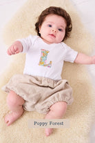 A smiling newborn baby wearing a personalised white bodysuit with an initial on the front cut from poppy forest floral  Liberty fabric.