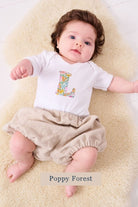 A smiling newborn baby wearing a personalised white bodysuit with an initial on the front cut from Liberty floral Poppy Forest fabric.