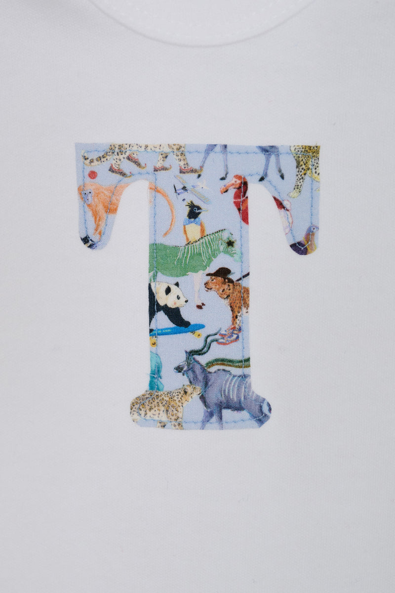 A close-up of a white baby grow personalised with a large letter 'T' printed with a Liberty quey 2  safari animal pattern, including a zebra, giraffe, panda, and cheetah, on a white background.