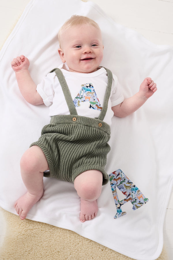 a smiling baby wearing a personalised baby bodysuit made from Liberty zoo animal print Quey 2 on a matching personalised blanket