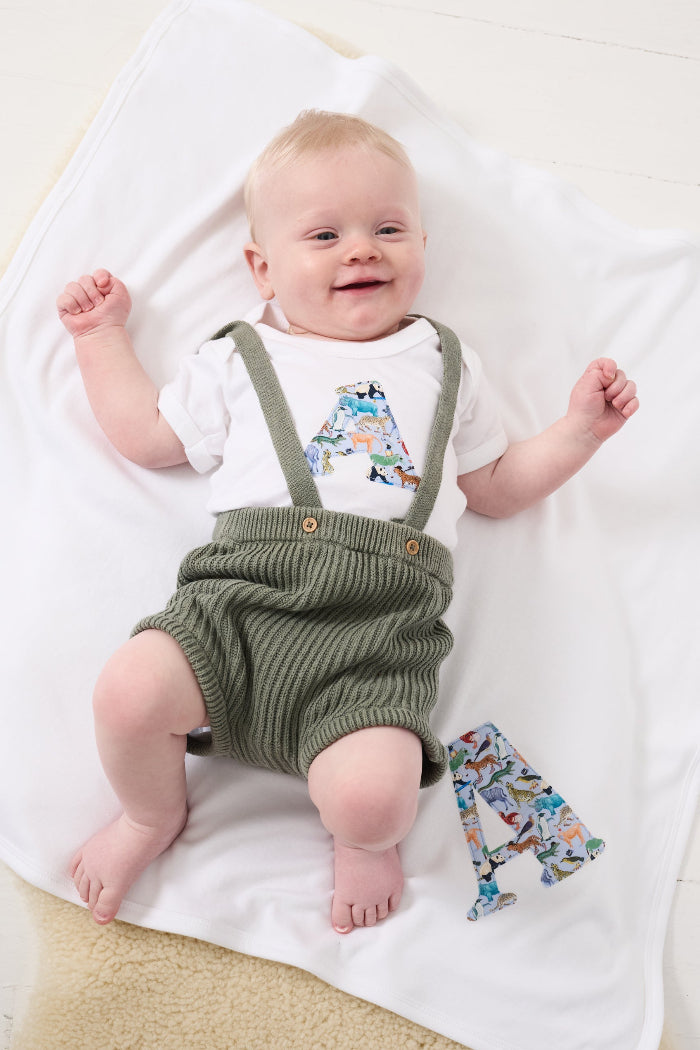 A newborn baby laying on Personalised Liberty Print Cotton Baby Blanket with their initial sewn on it.