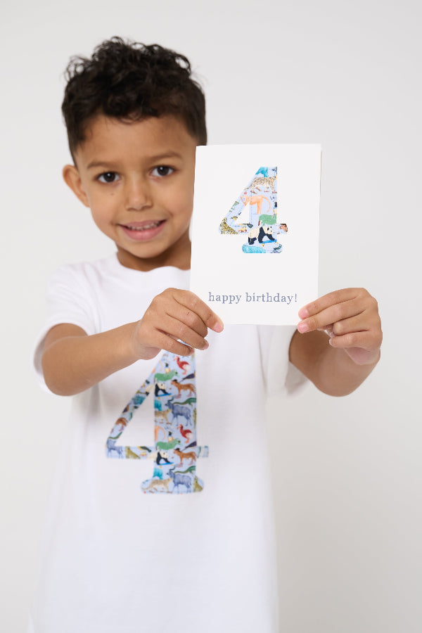 A 4 year old boy wearing a white cotton t-shirt with the number 4 sewn on the front cut from liberty Quey 2 zoo animal print. He is holding a matching number 4 birthday card