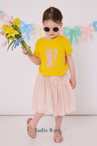 a 3 year old girl wearing a personalised kids yellow t-shirt with an initial cut from sadie rose liberty floral print on the front
