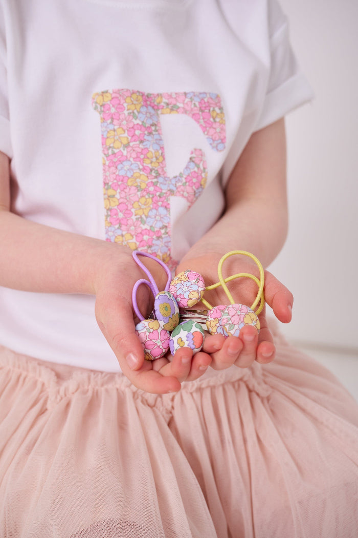 a little girl's hands holding liberty print hair clips and hair bobble elastics 