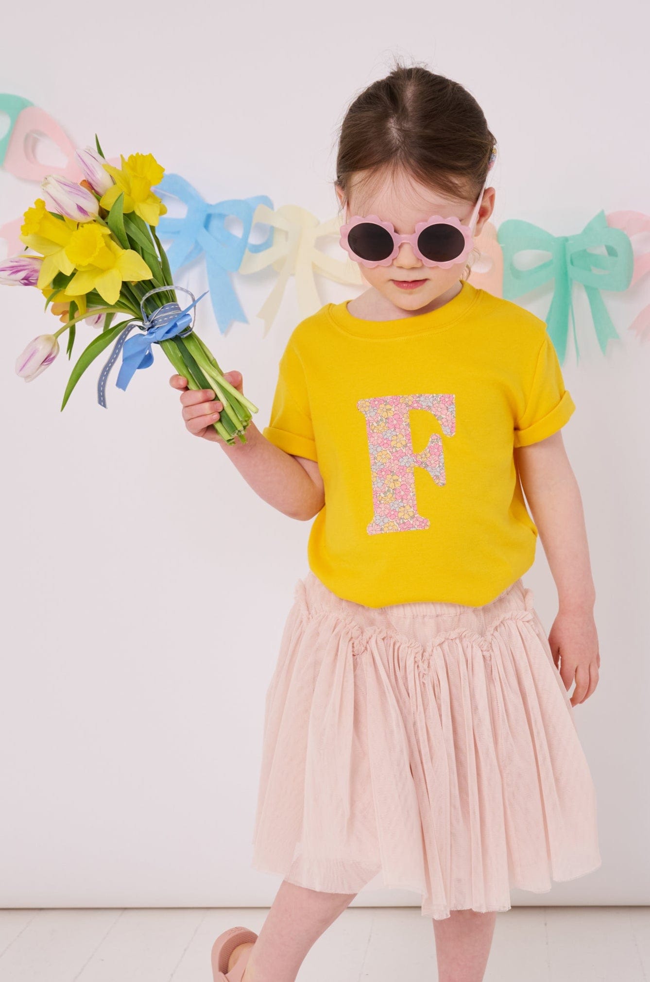 a 3 year old girl wearing a personalised kids yellow t-shirt with an initial cut from sadie rose liberty floral print on the front